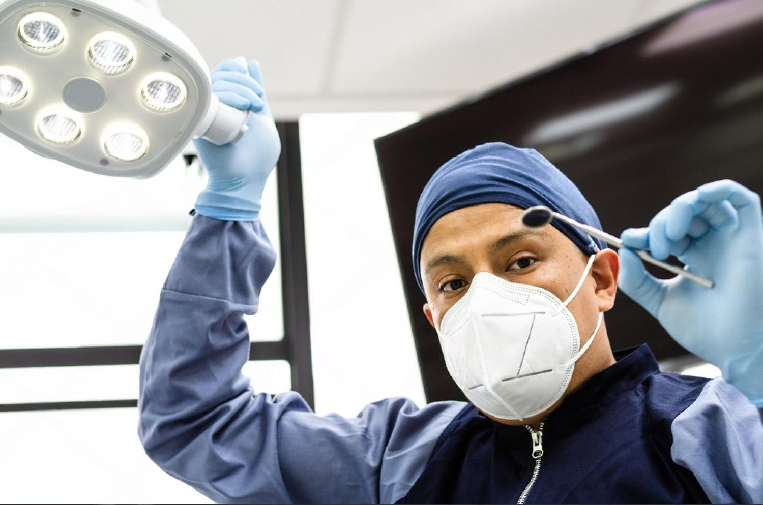 Dental intern in scrubs adjusting an overhead surgical lamp before a procedure